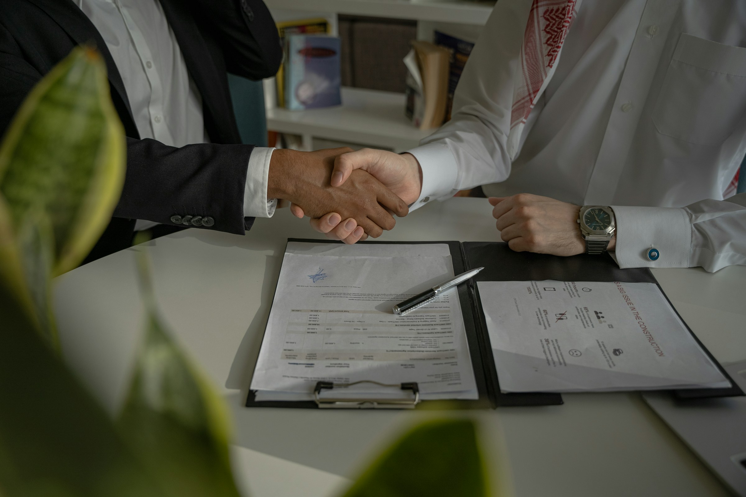 Two people shaking hands over a signed contract at a meeting table